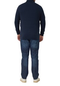 Marineblauer gestrickter Pullover mit Polokragen, langen Ärmeln und gerippten Bündchen. Kombiniert mit blauen Jeans und hellfarbenen Sneakers.