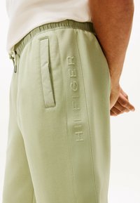 Jasnozielone dresowe spodnie sportowe wykonane z miękkiego materiału, z elastycznym paskiem w talii, bocznymi kieszeniami i wytłoczonym logo "HILFIGER" na nogawce.