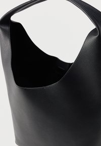 Μαύρη δερμάτινη τσάντα ώμου με ανάγλυφη υφή, ευρύ χερούλι και ευρύχωρο ανοιχτό πάνω μέρος, σε απλό ανοιχτό φόντο.