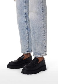 Sorte platform loafers med glat læderfinish og tyk gummisål, kombineret med lyseblå cowboybukser.