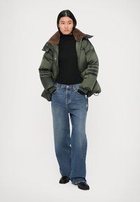 Doudoune vert foncé avec un col marron, associée à un pantalon en denim bleu ample et des chaussures noires. Design simple et moderne.