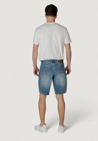 Shorts de mezclilla en azul claro, con un corte recto, bolsillos traseros y una etiqueta de cuero marrón en la cinturilla. Combinados con una camiseta blanca.
