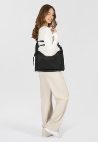 Sac en cuir noir avec une forme structurée, deux anses supérieures et une texture subtile, associé à un pantalon clair et des chaussures décontractées.