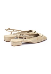 Chaussures slingback en suède beige avec un petit talon bloc, présentant un détail en nœud sur le devant et une sangle ajustable pour un maintien sécurisé.