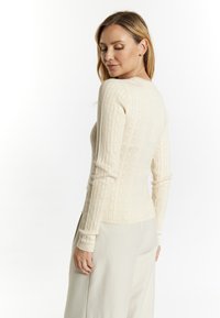 Lichtbeige gebreid top met geribbelde textuur en lange mouwen, met een aansluitende pasvorm en ronde halslijn, gedragen met crèmekleurige broeken.