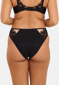 Sous-vêtements noirs avec des accents en dentelle florale sur les hanches, une texture lisse, un design taille haute et des panneaux semi-transparents sur les côtés.