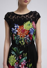 Kleid mit Blumendruck auf schwarzem Grund, mit Spitzenpasse, leuchtend bunten Blumenmustern und einem taillierten Schnitt mit Kordelzug.
