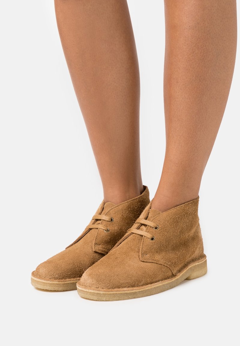 Botas de tobillo de ante en color marrón claro con punta redondeada, dos ojales para los cordones y una suela de goma en un tono marrón claro contrastante. Acabado de superficie texturizada.