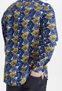 Camisa de manga larga con fondo azul, flores amarillas y follaje blanco, confeccionada en tejido ligero y con un corte relajado.