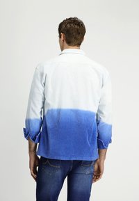 Blauw en witte gestreepte shirt met een dip-dye effect dat overgaat van licht naar donkerblauw. Voorzien van een kraag en opgerolde mouwen.