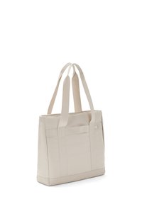 Beige színű tote táska, két erős pánttal, téglalap alakú, sima textúrával, elülső zsebbel és megerősített aljúval.