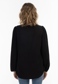 Zwarte blouse met lange mouwen en opgeblazen schouders, gladde textuur, ronde zoom en subtiele details op de mouwen. Gecombineerd met denim.