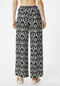 Mustavalkoiset kuviolliset leveälahkeiset housut, jotka on valmistettu kevyestä kankaasta. Ominaisuuksiin kuuluu joustava vyötärö ja laineileva siluetti.