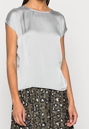 Woman wearing a light gray satin short-sleeve blouse and a dark green patterned skirt with floral and lace details.