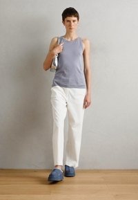 Gray sleeveless top, white tapered pants, and blue slip-on shoes. Silver handbag and large hoop earrings. Minimalist design with soft textures.