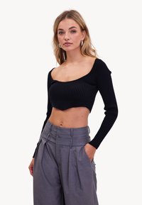 Zwarte geribbelde crop top met lange mouwen en een brede ronde halslijn, gecombineerd met grijze hoogstaande plooibroek.