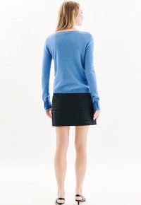 Hellblauer Pullover mit langen Ärmeln und gerippten Bündchen, kombiniert mit einem schwarz-karierten Minirock. Glatte Textur, schlichtes Design.