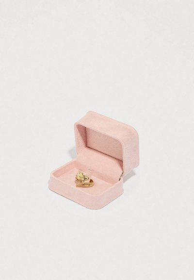 Różowe welurowe pudełko na biżuterię otwarte, z pokazanym złotym pierścionkiem z motywem lwa i obrączką przypominającą łańcuch, na białym tle.