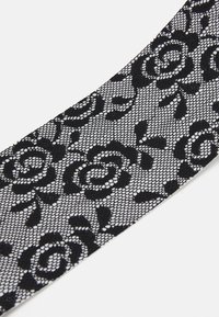 Un ruban en dentelle noire présentant un motif floral avec des roses. Le design a une texture semblable à un filet et mesure environ 5 cm de large.