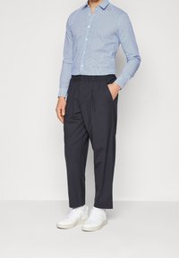 Camisa de patrón azul claro con mangas largas, pantalones ajustados en azul marino y zapatillas blancas. Incluye una cintura elástica y bolsillos laterales.
