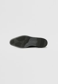 Semelle de chaussure noire avec une finition texturée en caoutchouc. Présente un motif de semelle pour l'adhérence et un léger talon surélevé.
