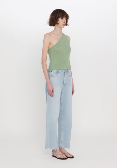 Grön, strukturerad top med en axel, kombinerad med ljusblå, vida jeans med fransar i nederkant och svarta platta sandaler med fina remmar.