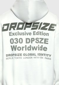 Hoodie blanc avec texte noir au dos indiquant "DROPSIZE Édition Exclusive 030 DPSZE Monde entier" et noms de villes Berlin, Tokyo, Londres, New York, Paris.