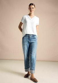 T-shirt bianco a scollo a V, jeans azzurri a vestibilità rilassata con risvolti, e scarpe marroni slip-on; tessuto morbido e design casual.