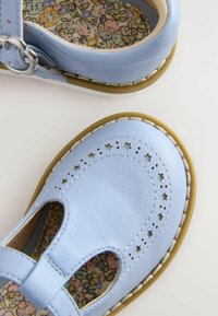 Zapatos de cuero azul claro con patrones de estrellas perforadas. Cuentan con un diseño de tira en T y una plantilla con patrón floral. Suela de goma con detalles cosidos.