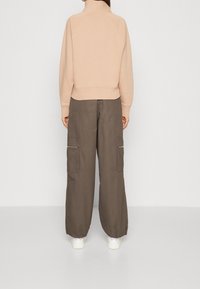 Sudadera beige con cremallera, cuello alto y dobladillo acanalado, combinada con pantalones cargo marrones de corte holgado con bolsillos con cremallera.