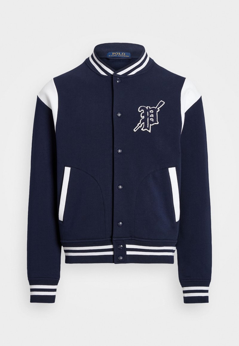 Chaqueta varsity azul marino con acentos blancos, cuello y puños acanalados, con un logo en el frente y dos bolsillos laterales. Textura de tela suave.