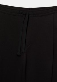 Schwarze Jogginghose mit elastischem Bund, ausgestattet mit einer Kordelzug-Detail und Seitentaschen. Glatte Textur und schlichtes Design.