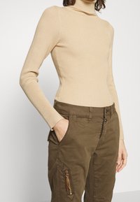 Beige ribbad polokrage med långa ärmar, matchad med olivgröna cargobyxor med sidodragkedjeficka och diskret sömnadsdetalj.