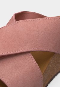 Κοντινό πλάνο ροζ σουέτ πέδιλου με φαρδιές σταυρωτές λουριά και πάτο τύπου φελλού.