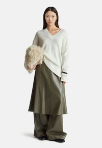 Weißer, strukturierten Pullover mit V-Ausschnitt und geripptem Saum, kombiniert mit einem olivgrünen, glänzenden Lederrock und einer flauschigen, cremefarbenen Handtasche.