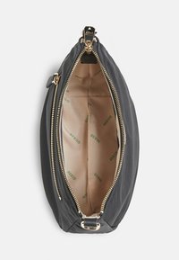 Sort nylon håndtaske med en glat tekstur, guldfarvet lynlås og beige indvendig foring med et gentagende grønt logomønster.
