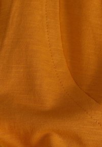 Tela naranja con una textura suave, que presenta sutiles detalles de costura y un borde curvado, resaltando su diseño ligero.