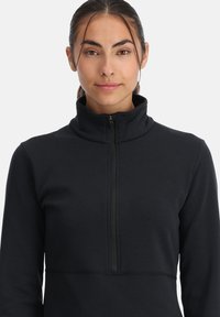 Zwarte fleece pullover met een hoge kraag en een quarter-rits. Glad textuur, getailleerd ontwerp en versterkte stiksels aan de zoom.