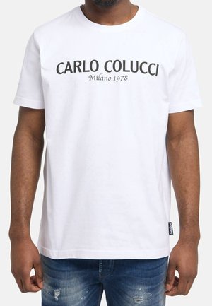 White cotton t-shirt with short sleeves, featuring bold black text "CARLO COLUCCI Milano 1978" across the chest. Distressed blue jeans visible.