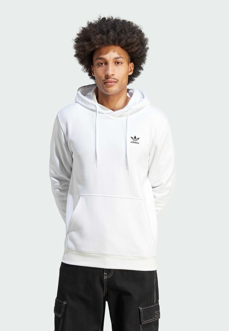 Felpa bianca in cotone con cappuccio e cordini, tasca frontale a marsupio e logo Adidas nero sul petto. I pantaloni cargo neri completano l'outfit.