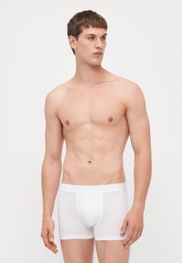 Weiße Baumwollboxershorts mit einem weichen Bund, figurbetonter Passform und glatter Textur, die einen minimalistischen Stil und klare Linien präsentieren.