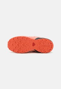 Under-sole of a running shoe featuring a textured, orange rubber outsole with pronounced lugs for traction, and black accents on the heel.