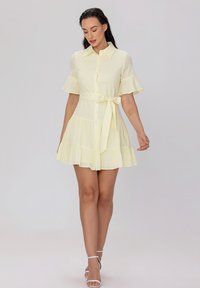 Robe jaune à manches courtes avec un devant à boutons, taille cintrée et jupe évasée, dotée d'une ceinture à nouer et d'un matériau texturé.