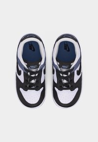 Ζευγάρι παπουτσιών Nike σε μαύρο, λευκό και γκρι χρώμα με μαύρα κορδόνια, μπλε εσωτερικές σόλες και το λογότυπο της Nike ορατό στο εσωτερικό και στη γλώσσα των παπουτσιών.