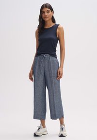 Top senza maniche blu navy abbinato a pantaloni ampi di colore azzurro chiaro, simili al lino, con vita regolabile e aperture laterali. Le sneakers completano il look.