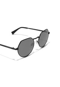 Crne osmerokutne sunčane naočale s tamnim staklima, metalnim okvirom i tankim krakovima. Imaju jastučić za nos i ugravirani brend na kraku.