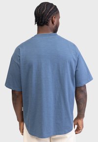 Loose-fit, short-sleeve t-shirt in muted blue fabric. Features a round neckline and side slits. Smooth texture, minimal branding.