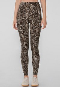 Legginsy w panterkę wykonane z elastycznego materiału, z wysokim stanem i dopasowanym krojem. Wzór składa się z ciemnobrązowych plam na jasnobrązowym tle.