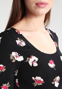 Haut noir à imprimé floral avec un décolleté arrondi, des manches courtes et un tissu texturé orné de motifs de fleurs blanches et roses.