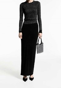 Schwarzer Strickpullover mit Schimmer, lange Ärmel. Passender schwarzer bodenlanger Rock. Schwarze verzierte Handtasche, spitze Absatzschuhe.